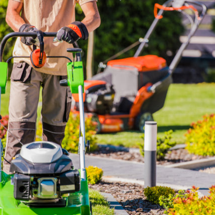 Lawn & LandscapeA landscaper standing behind a lawn mower with a riding mower in the background.