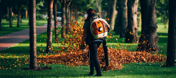 A woman holding a backpack leaf blower outside to clear leaves.